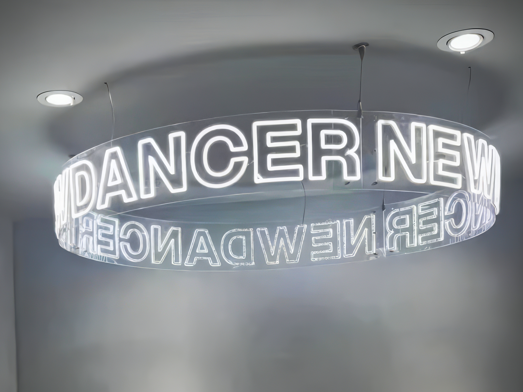 Custom cool white neon LED chandelier suspended from the ceiling in a dance studio featuring illuminated acrylic ring signage.
