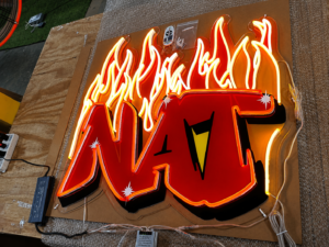 Custom LED neon logo sign with UV printed acrylic backing and flame graphics for business branding and interior display.