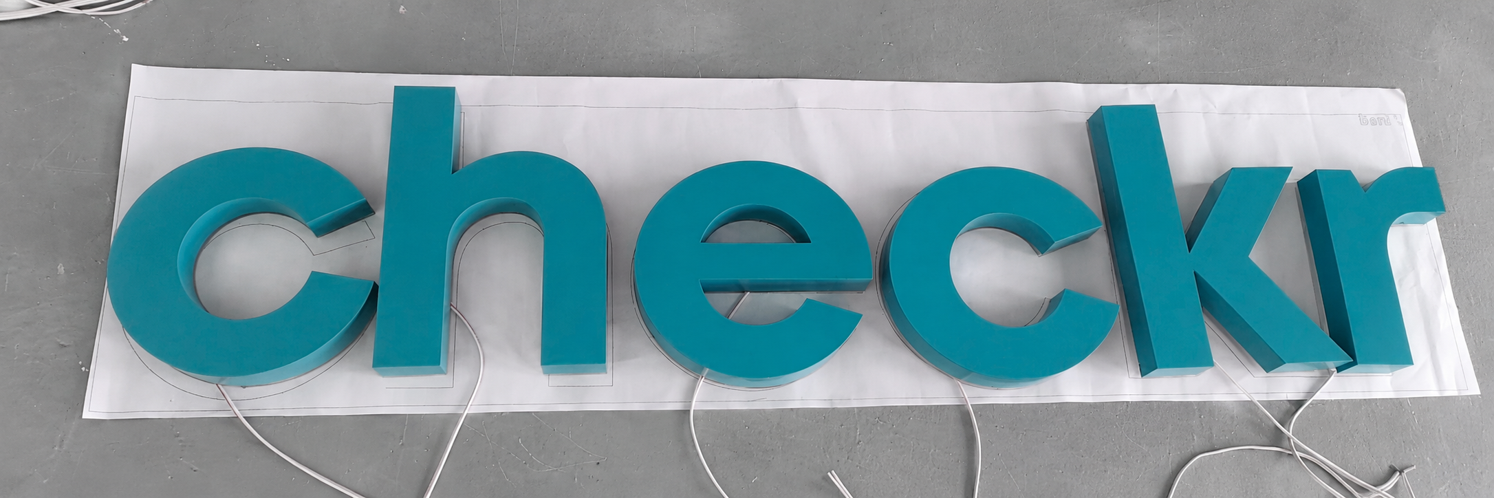 Teal Checkr reverse-lit logo letters arranged for production testing