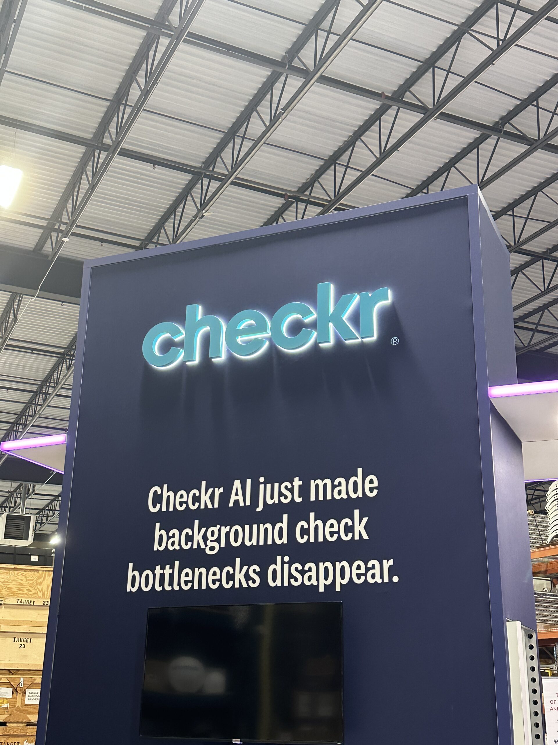 Installed teal Checkr halo-lit logo mounted on a trade show booth wall