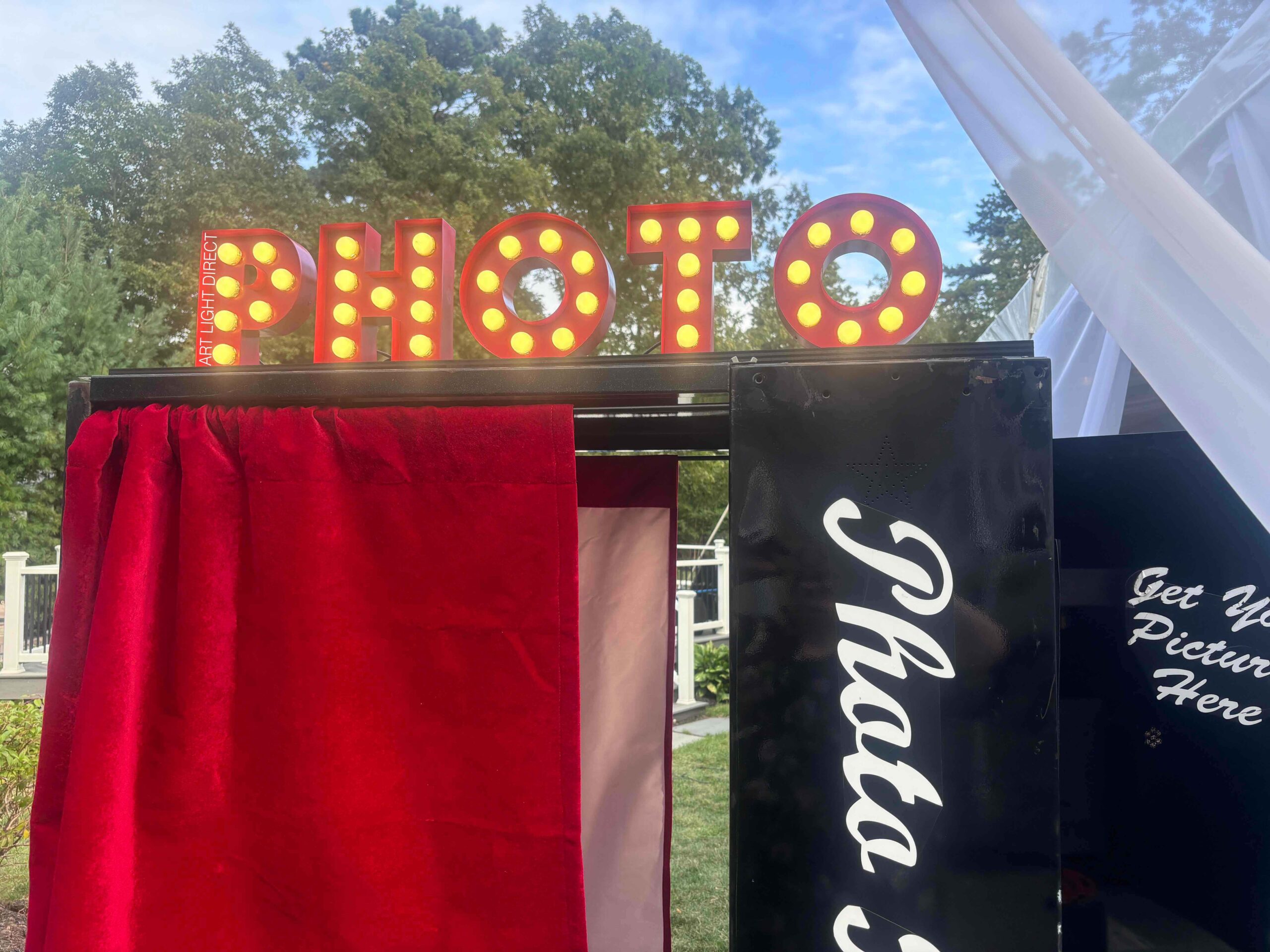 Close-up of a custom marquee photo booth sign with red PHOTO letters and warm exposed bulbs.