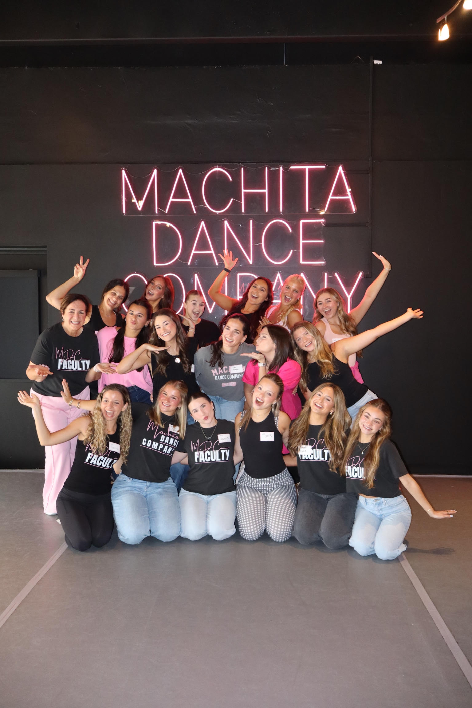 Machita Dance Company group celebrating in front of pink LED neon sign