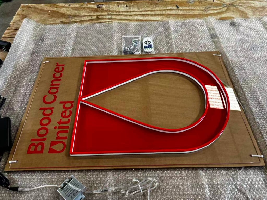 Blood Cancer United sign before packing, with UV-printed lettering and red logo panels outlined in LED neon.