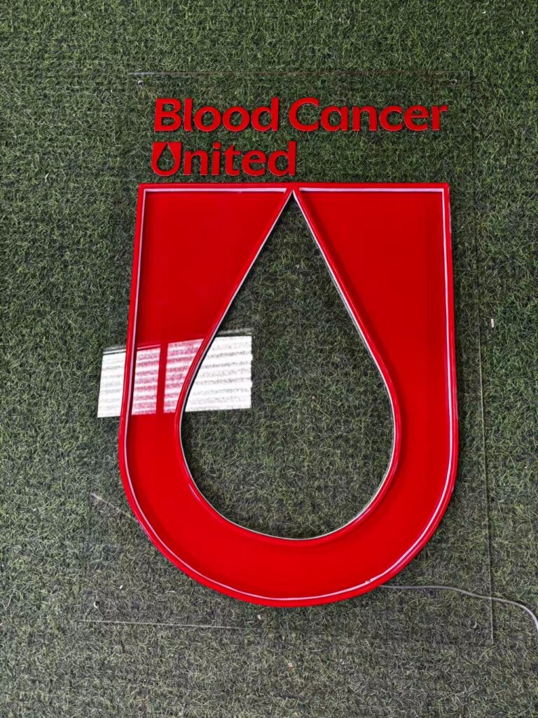 Blood Cancer United wording and red logo panels on a neon LED sign, displayed outdoors.