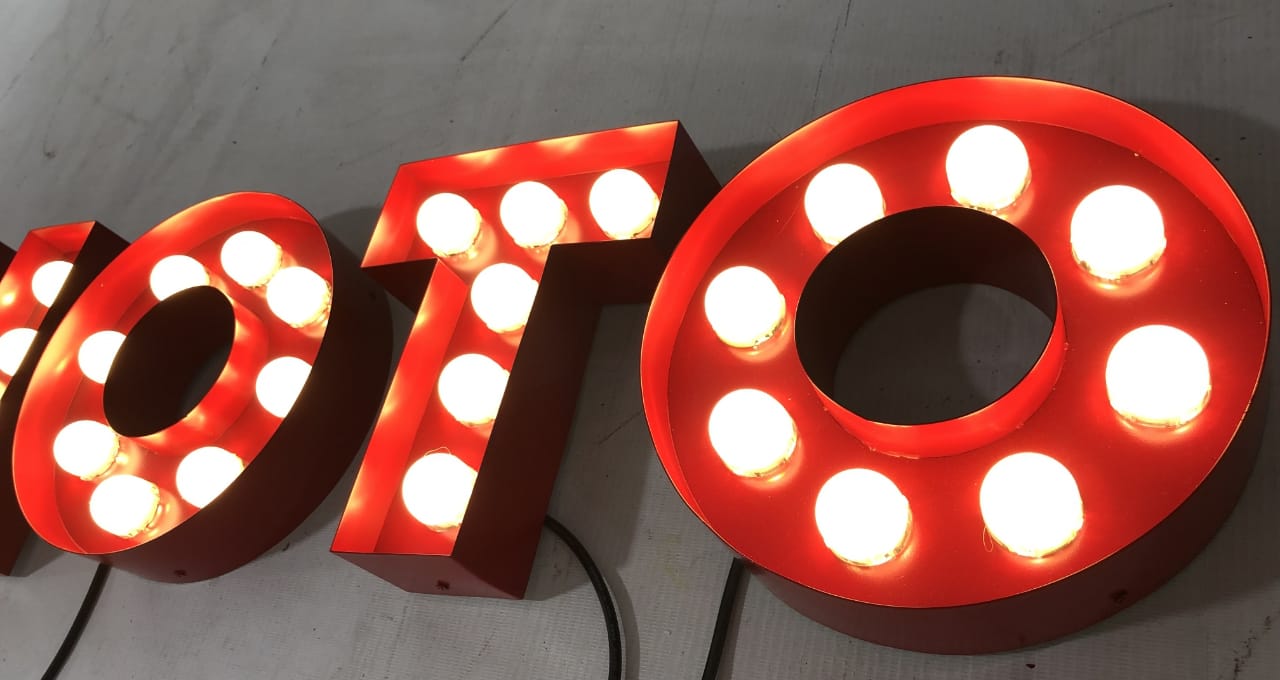 Angled close-up of red PHOTO marquee letters illuminated by warm white LED bulbs.